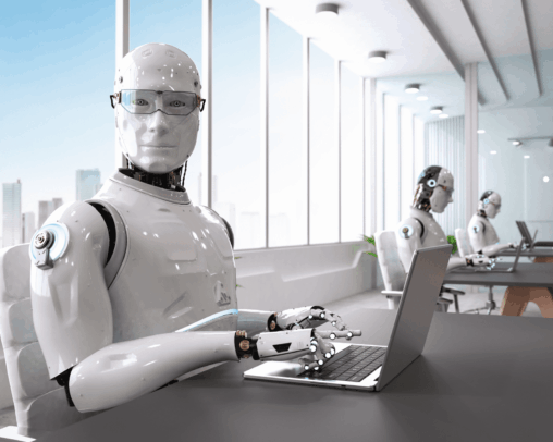 A white humanoid robot with a fully featured but plastic face looks directly at the viewer, as if asked to fill out a billion TPS reports. Its back is to a bank of windows and 2 other robots at nearby tables. All are typing on their laptops.